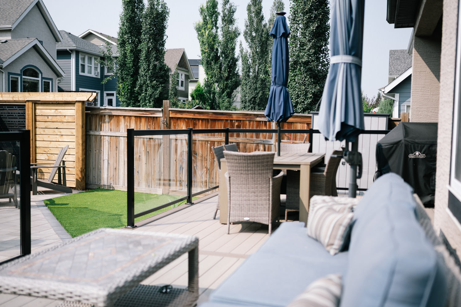 Calgary backyard featuring a modern deck with a dining area, privacy screens, and a grassy turf space, showcasing the Mahogony 1 landscaping project by Kayben Landscaping.
