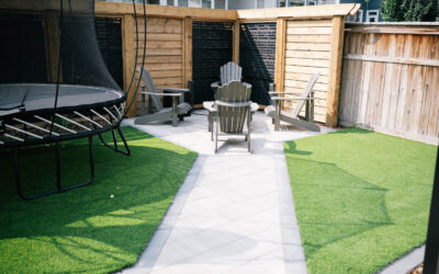 Outdoor seating area with patio stones, Adirondack chairs, and a trampoline, surrounded by wooden fencing and artificial grass, showcasing a residential landscaping project by Kayben Landscaping.