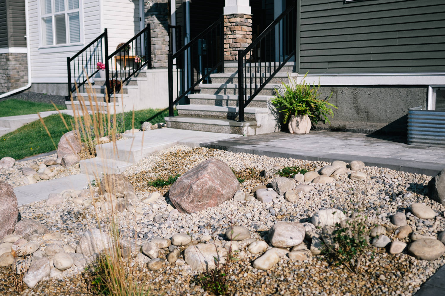 Xeriscape front yard featuring decorative rocks, gravel, and ornamental grasses surrounding a modern home entrance with steps and railing.