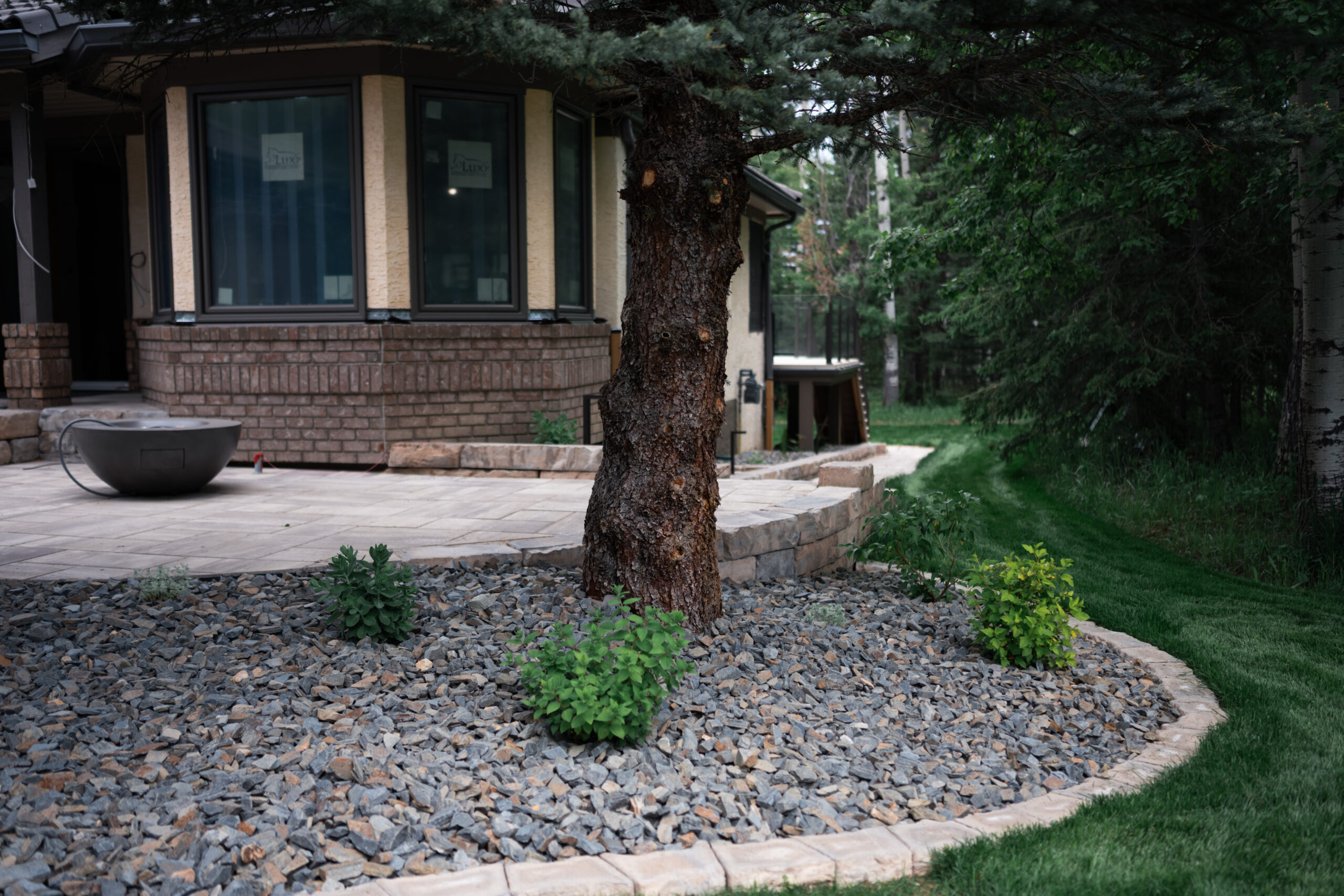 Landscaped patio area featuring stone pavers, a decorative fire bowl, and surrounding greenery in Priddis Greens, showcasing Kayben Landscaping's outdoor design expertise.