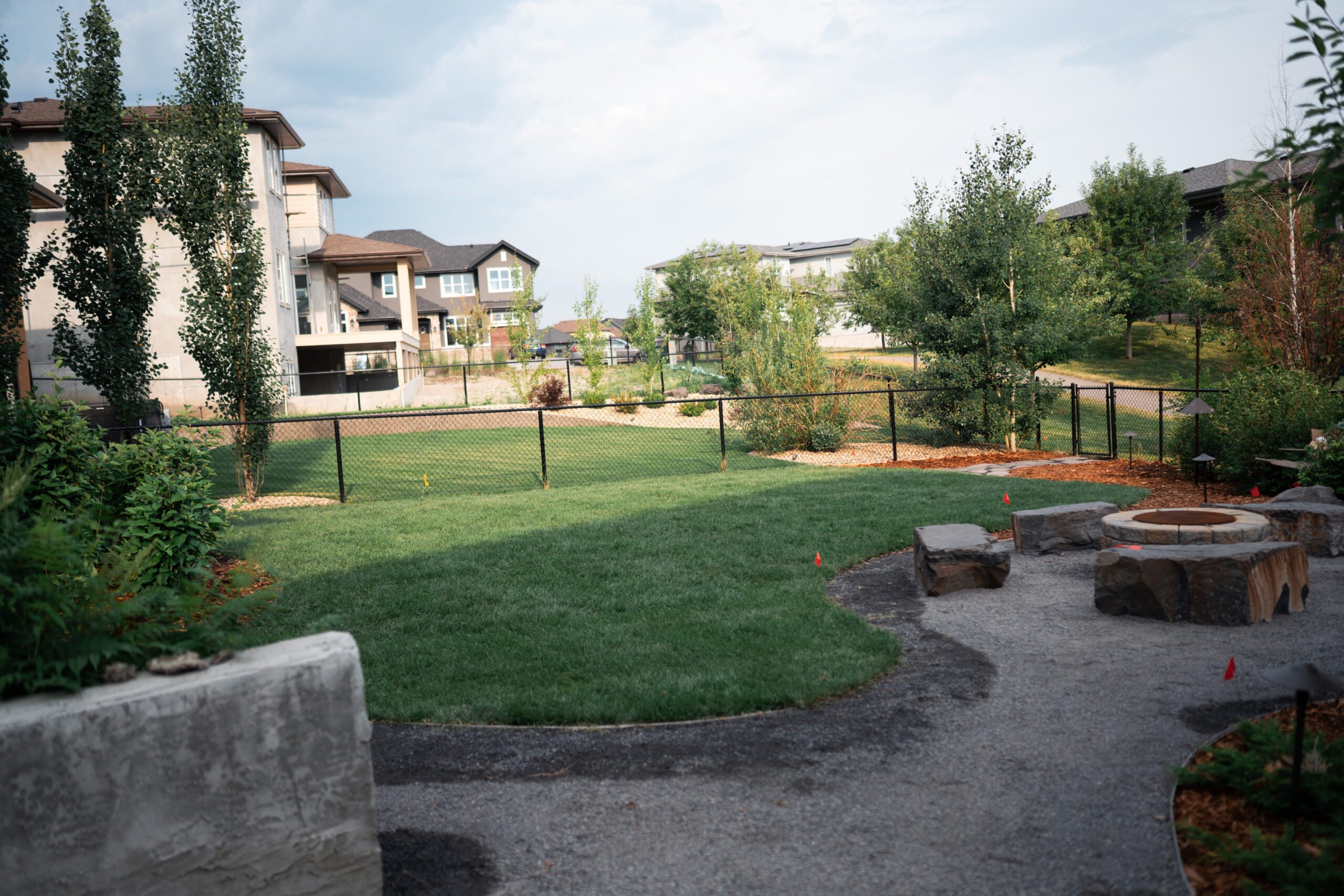 Landscaped yard at Artesia at Heritage Pointe featuring sod, stone fire pit, and surrounding residential homes.