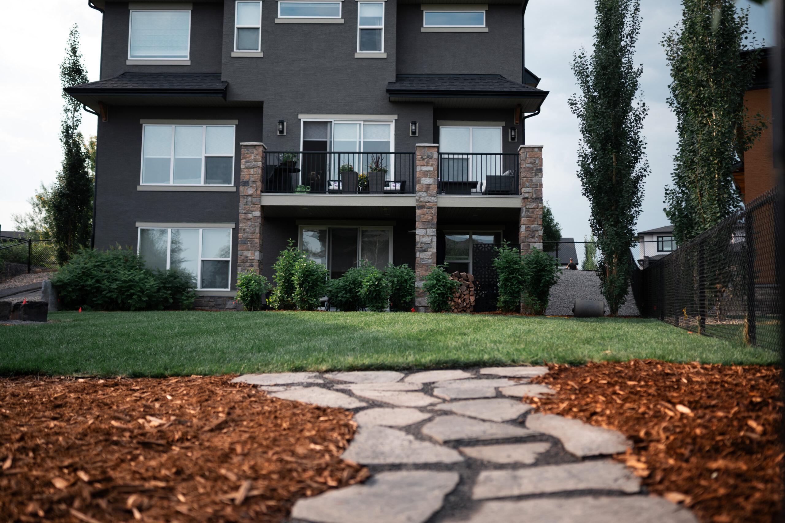Modern estate home with stone patio, landscaped yard featuring sod, decorative mulch, and greenery at Artesia at Heritage Pointe.