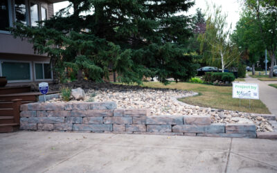Residential landscaping featuring a stone retaining wall, decorative rocks, and surrounding greenery, showcasing Kayben Landscaping's design work.