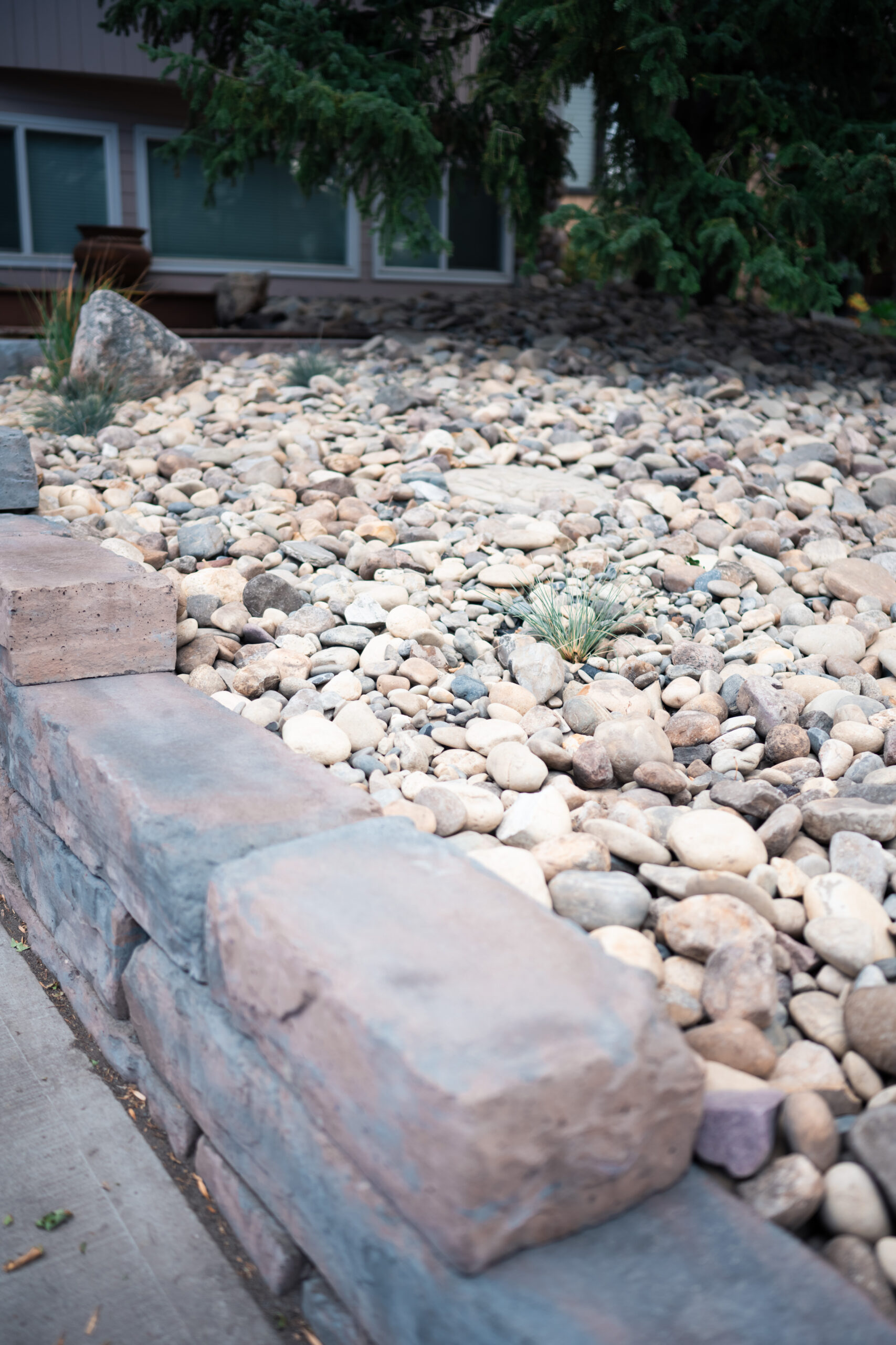 Xeriscape front yard featuring a custom retaining wall and river rock bed, designed for low maintenance in Okotoks.