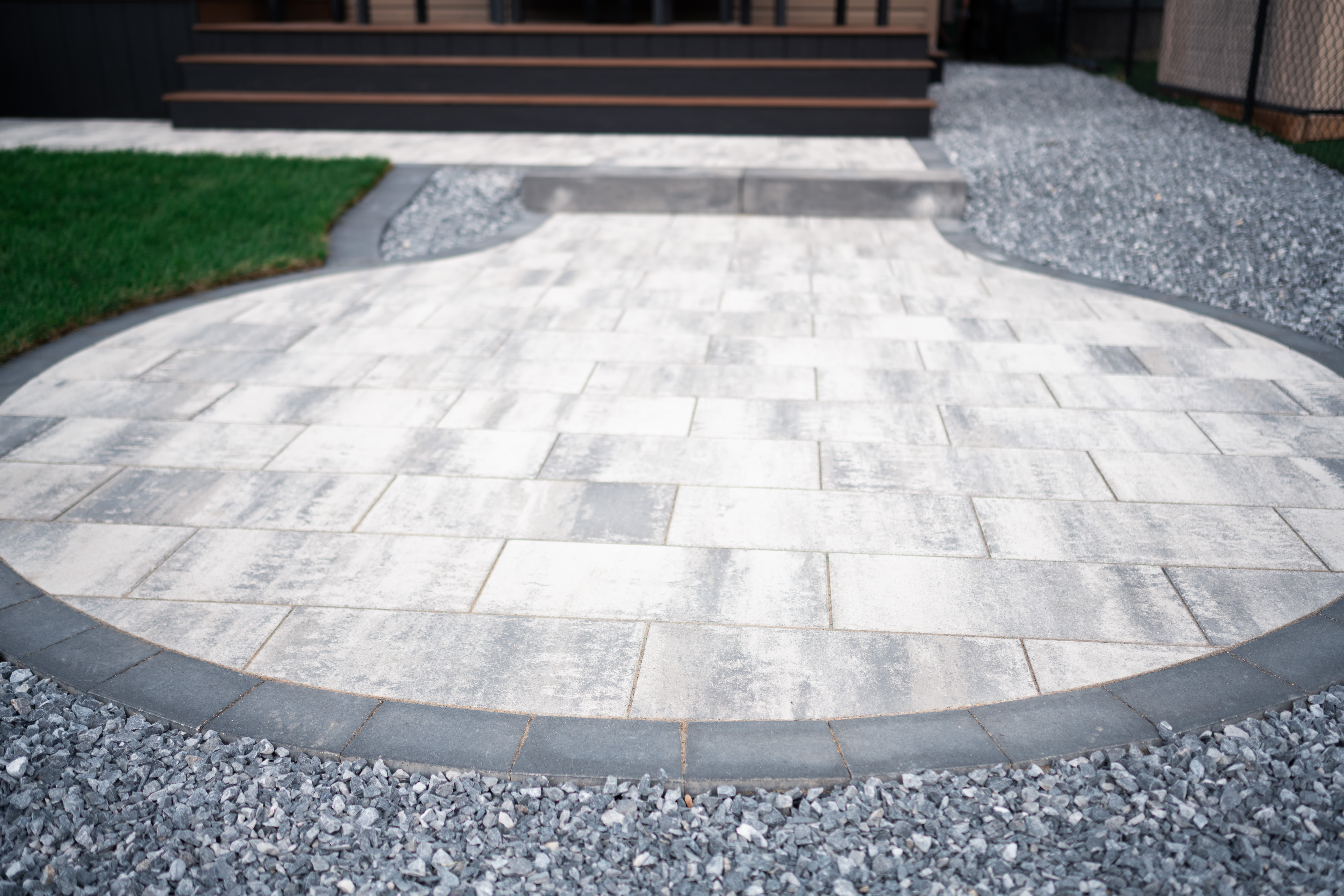 Paved patio area with gray stone tiles, bordered by gravel and green sod, showcasing landscaping design in Drake Landing, Okotoks.