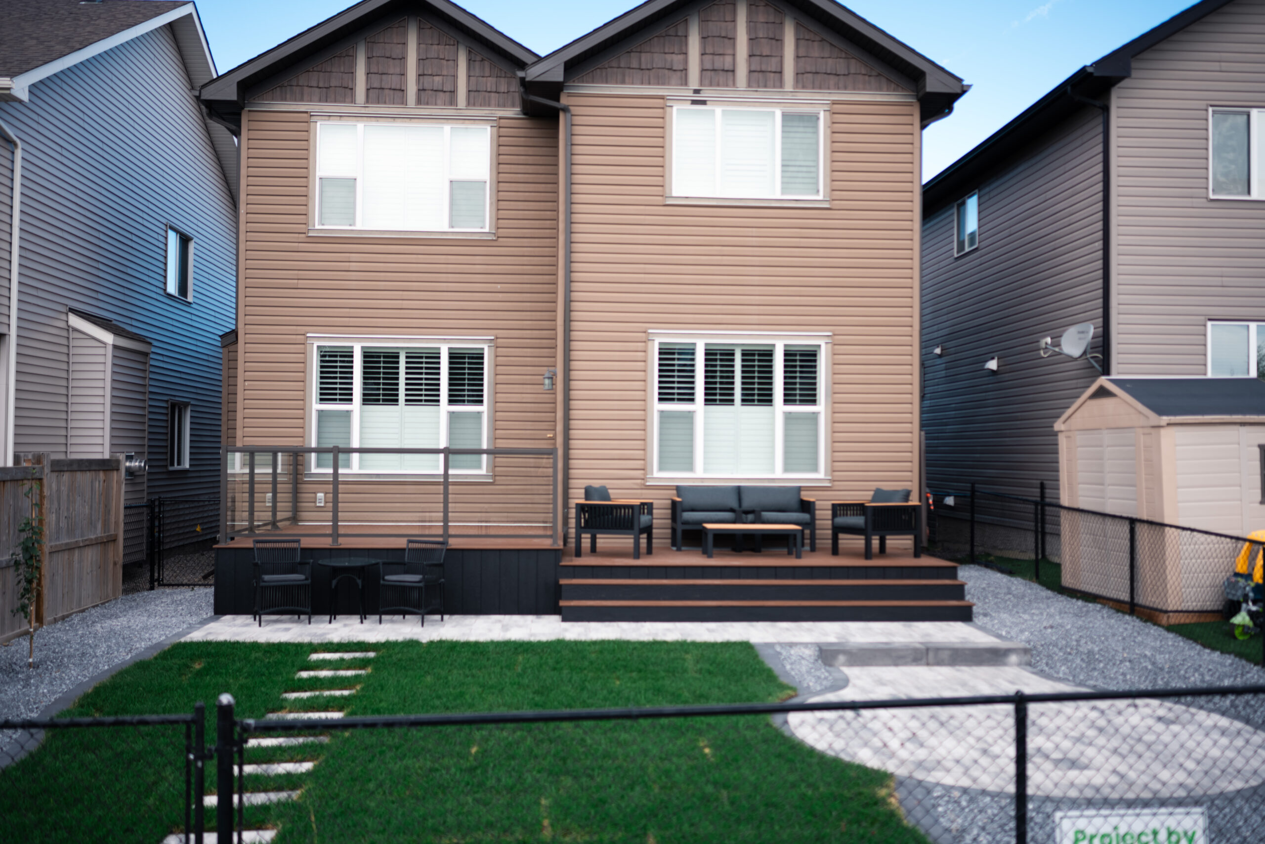 Residential home in Drake Landing with a wooden deck, modern seating area, and landscaped yard featuring sod and stepping stones.