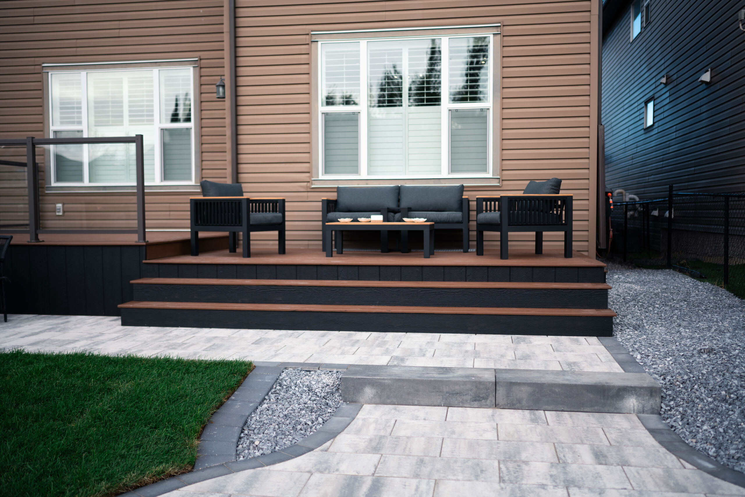 Residential patio with seating area, modern deck design, and landscaped pathway featuring grass and gravel, showcasing Kayben Landscaping's work in Drake Landing, Okotoks.