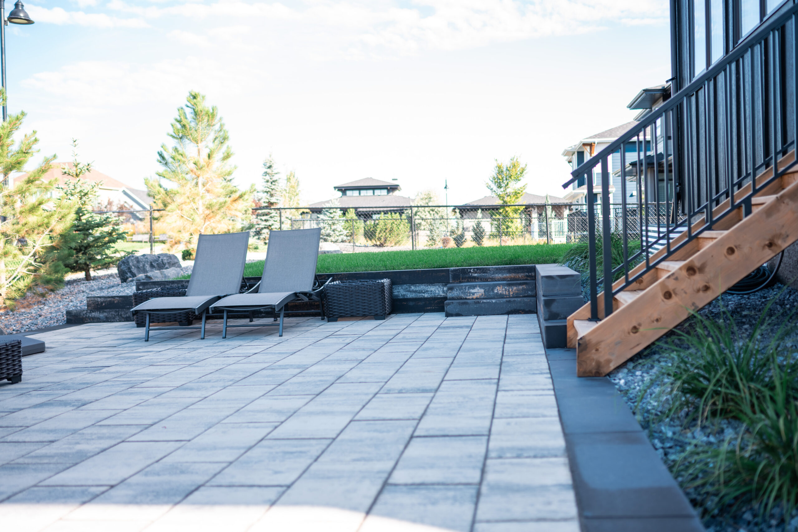 Outdoor seating area with gray lounge chairs on a paver patio, landscaped with grass and decorative stones, showcasing Kayben Landscaping's design in Artesia at Heritage Pointe.