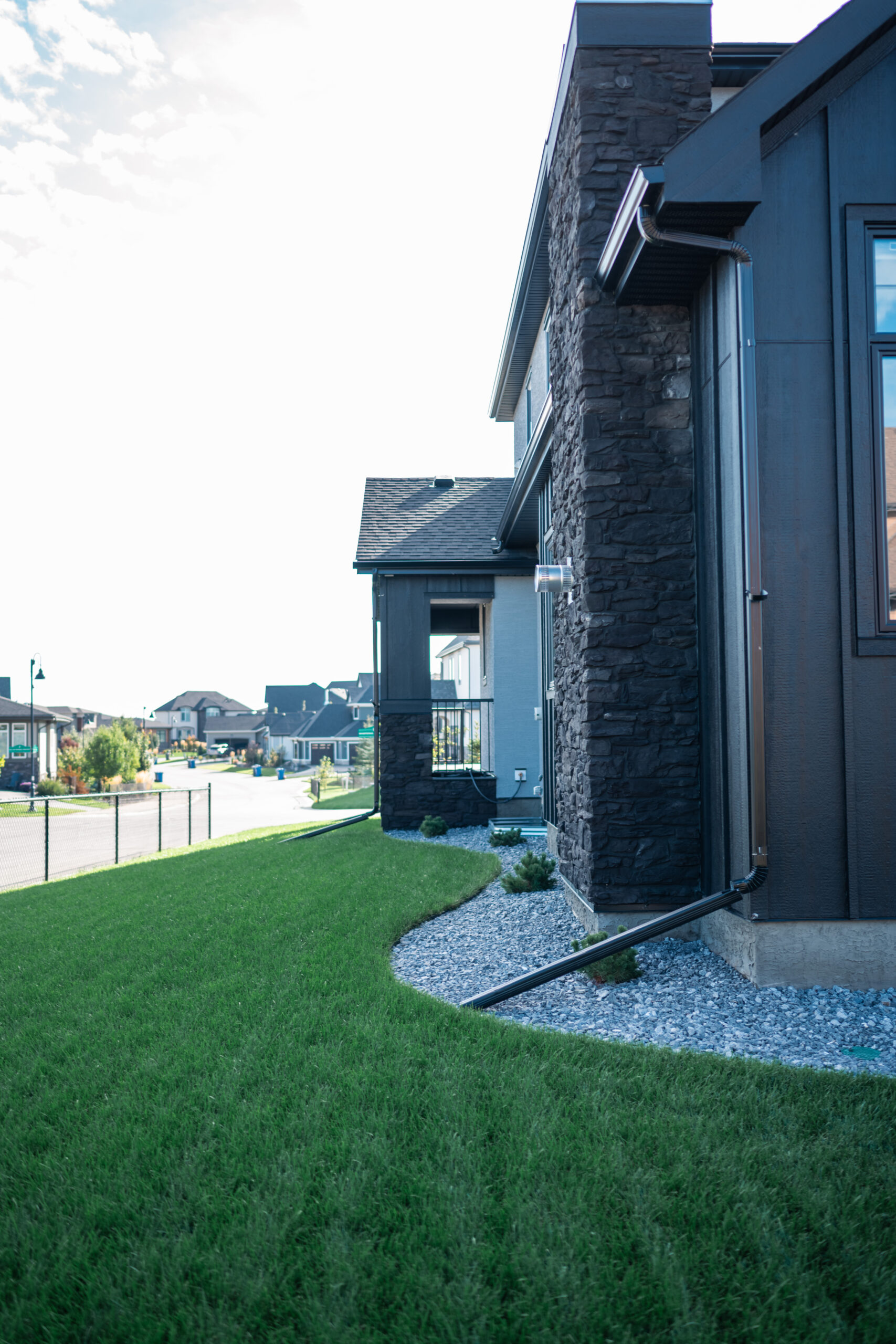 Side view of a modern home with stone accents, featuring a well-maintained green lawn, decorative gravel landscaping, and nearby residential streets in the Artesia at Heritage Pointe community.