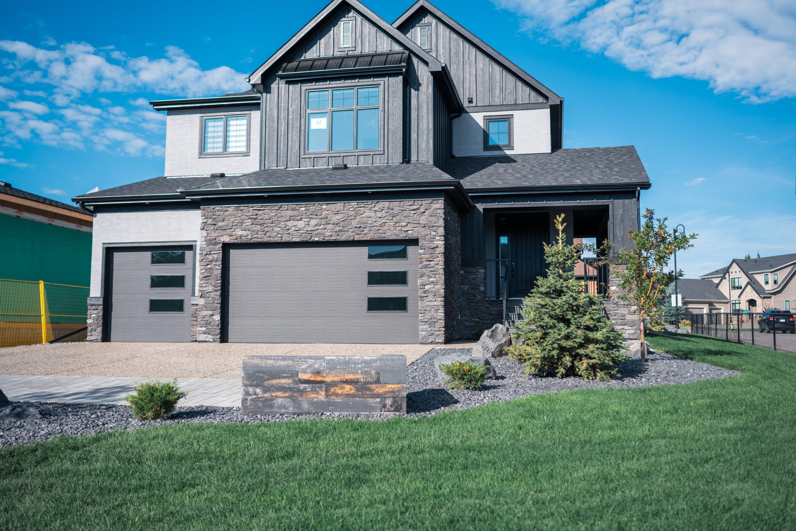 Modern estate home in Artesia at Heritage Pointe featuring stone accents, landscaped front yard with sod and decorative elements, showcasing Kayben Landscaping's expertise.