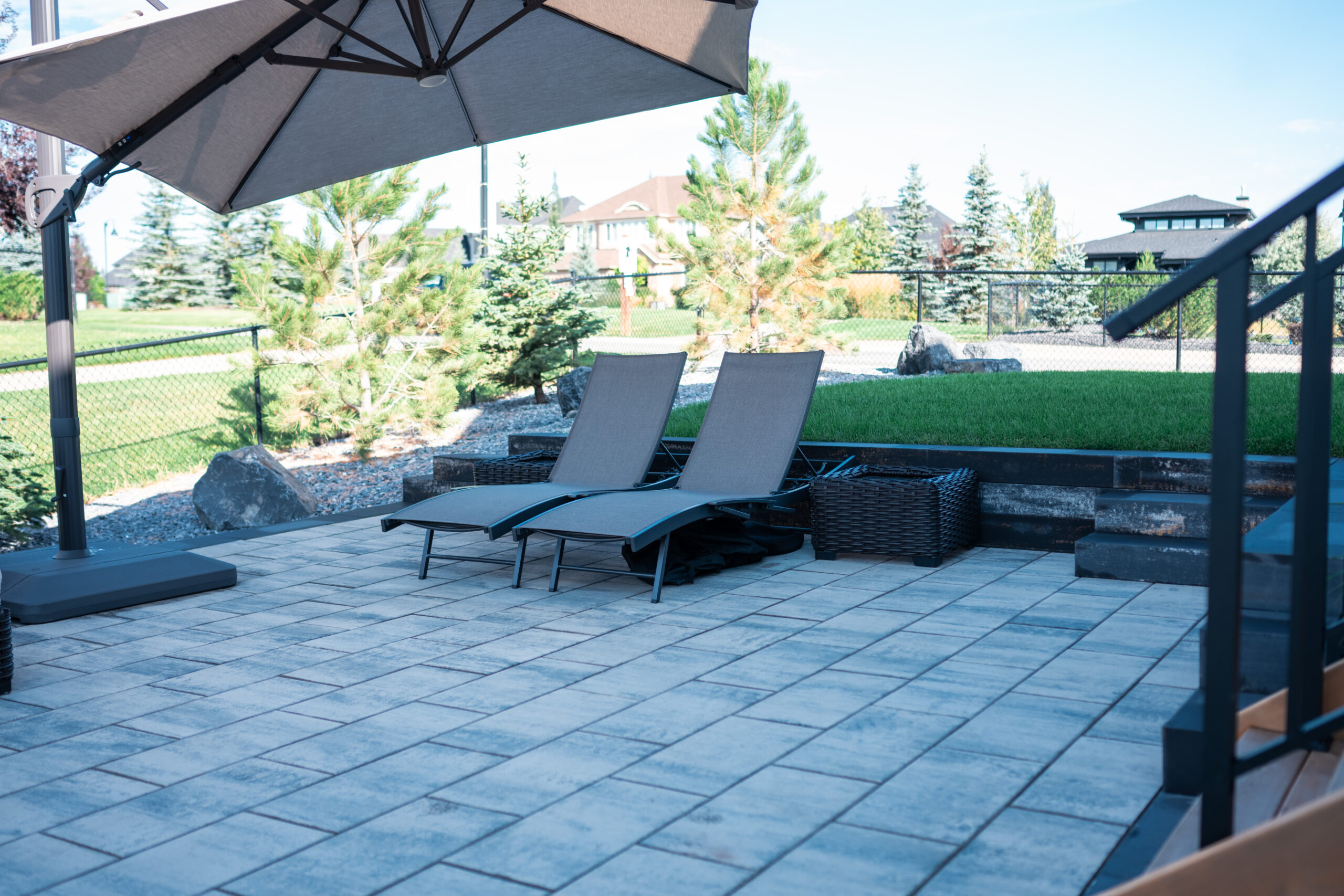 Seating area with two lounge chairs under an umbrella, surrounded by landscaped garden and paver patio in Artesia at Heritage Pointe.