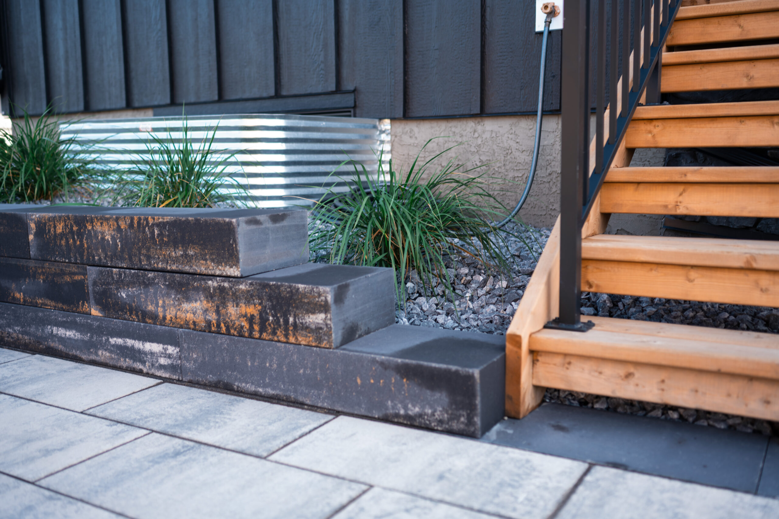 Black paver steps leading to wooden stairs, surrounded by decorative grasses and gravel, showcasing landscaping features in Artesia at Heritage Pointe.