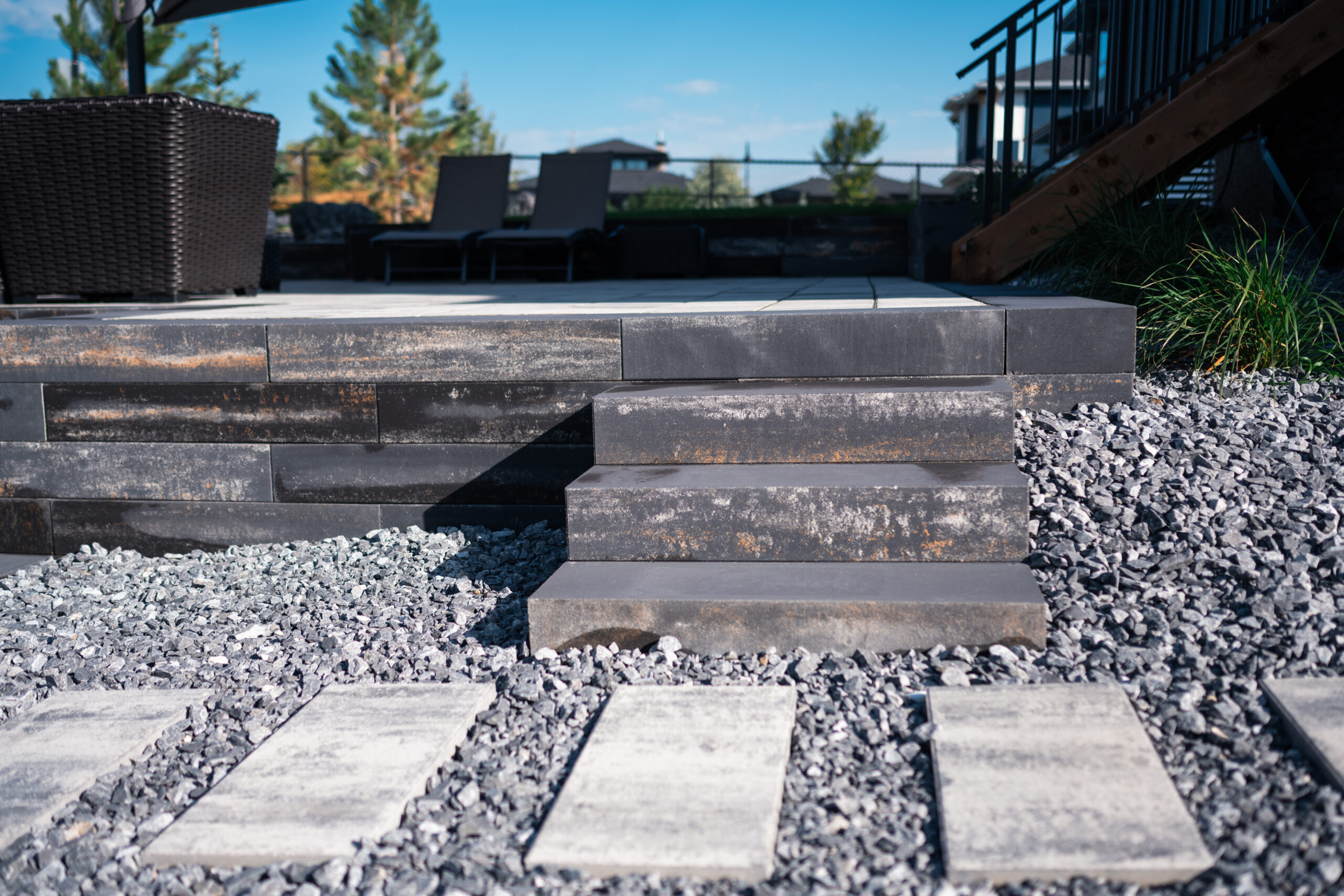 Patio steps with textured black pavers, surrounded by gravel and stone pathways, leading to a seating area in Artesia at Heritage Pointe landscaping project by Kayben Landscaping.