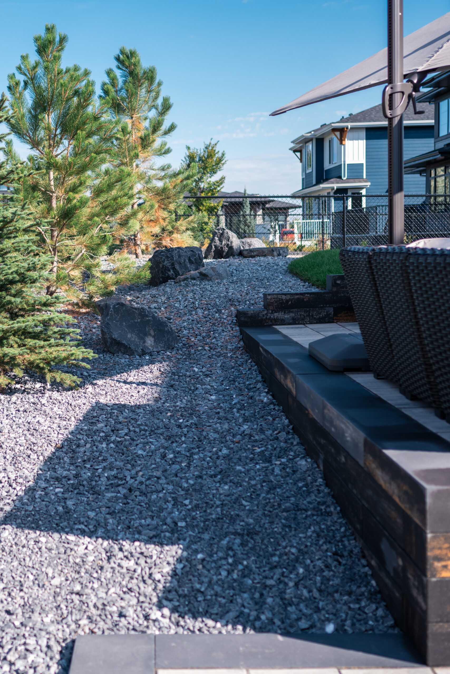 Landscaped pathway featuring gravel, pine trees, and a seating area with stone pavers in Artesia at Heritage Pointe, showcasing Kayben Landscaping's design expertise.