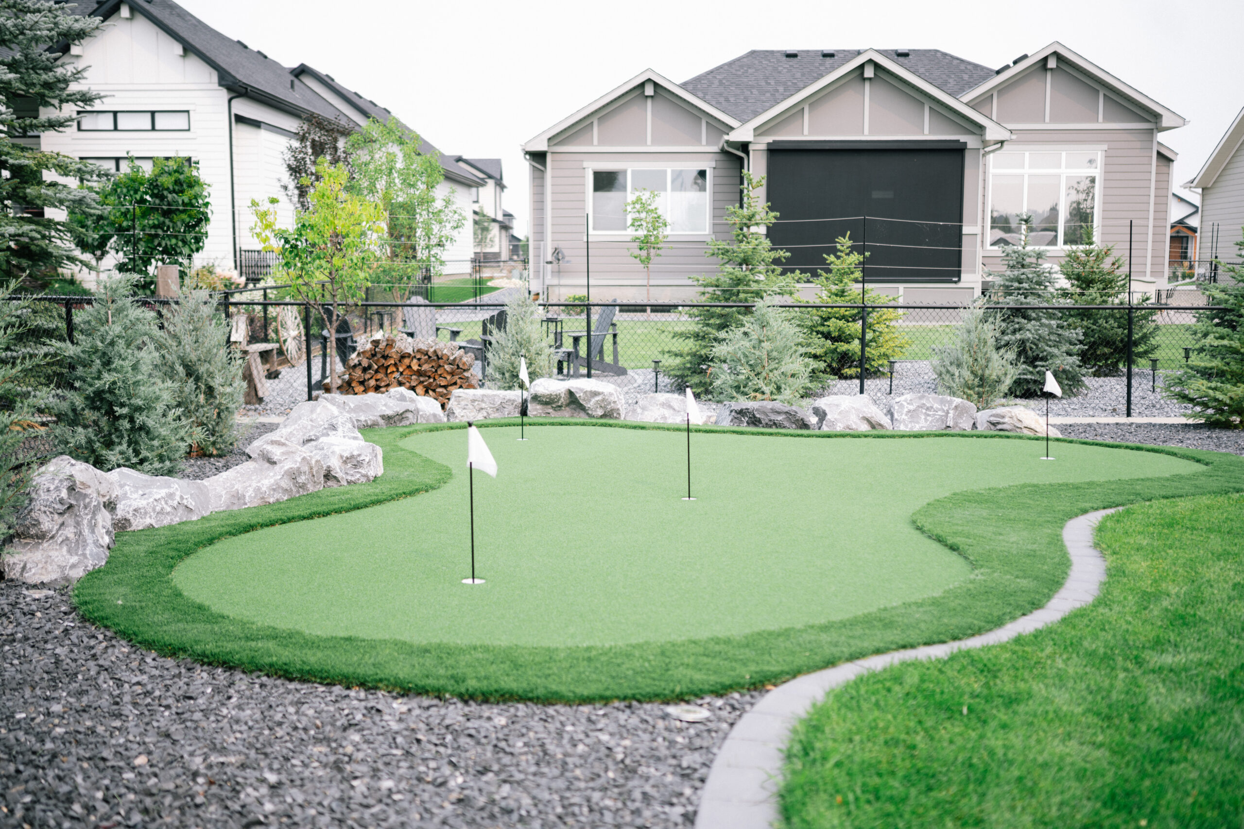 okotoks-cimarron-estates-putting-green-patio-seating Backyard putting green with turf, stone patio, seating area, and sod in Okotoks Cimarron Estates