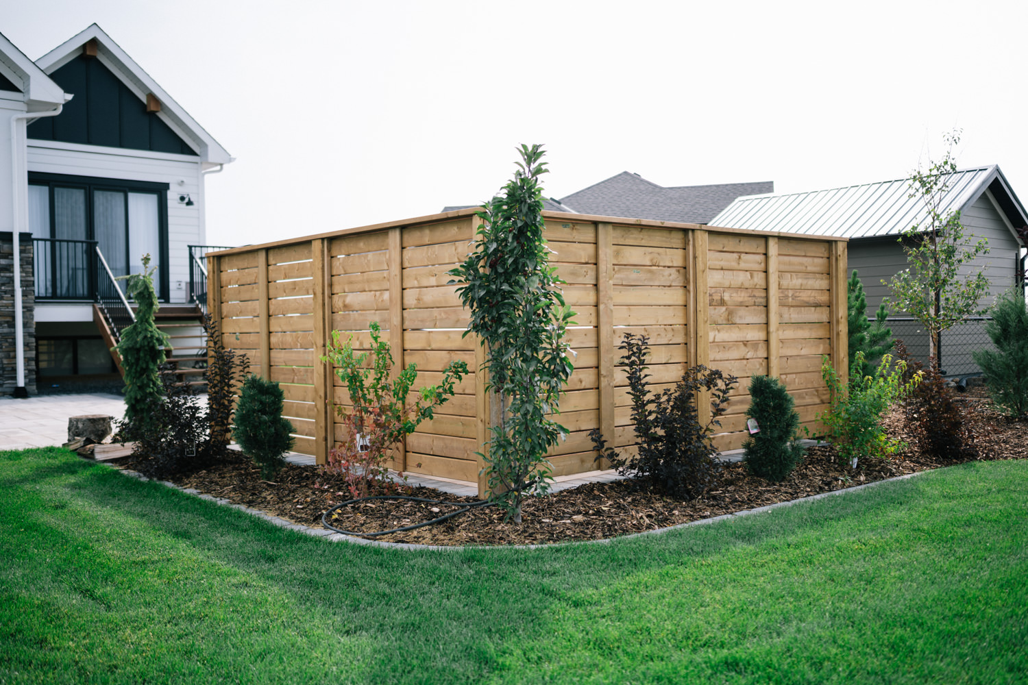 Wooden privacy screen surrounded by landscaped garden with various plants and grass, showcasing residential outdoor design in Green Haven area.