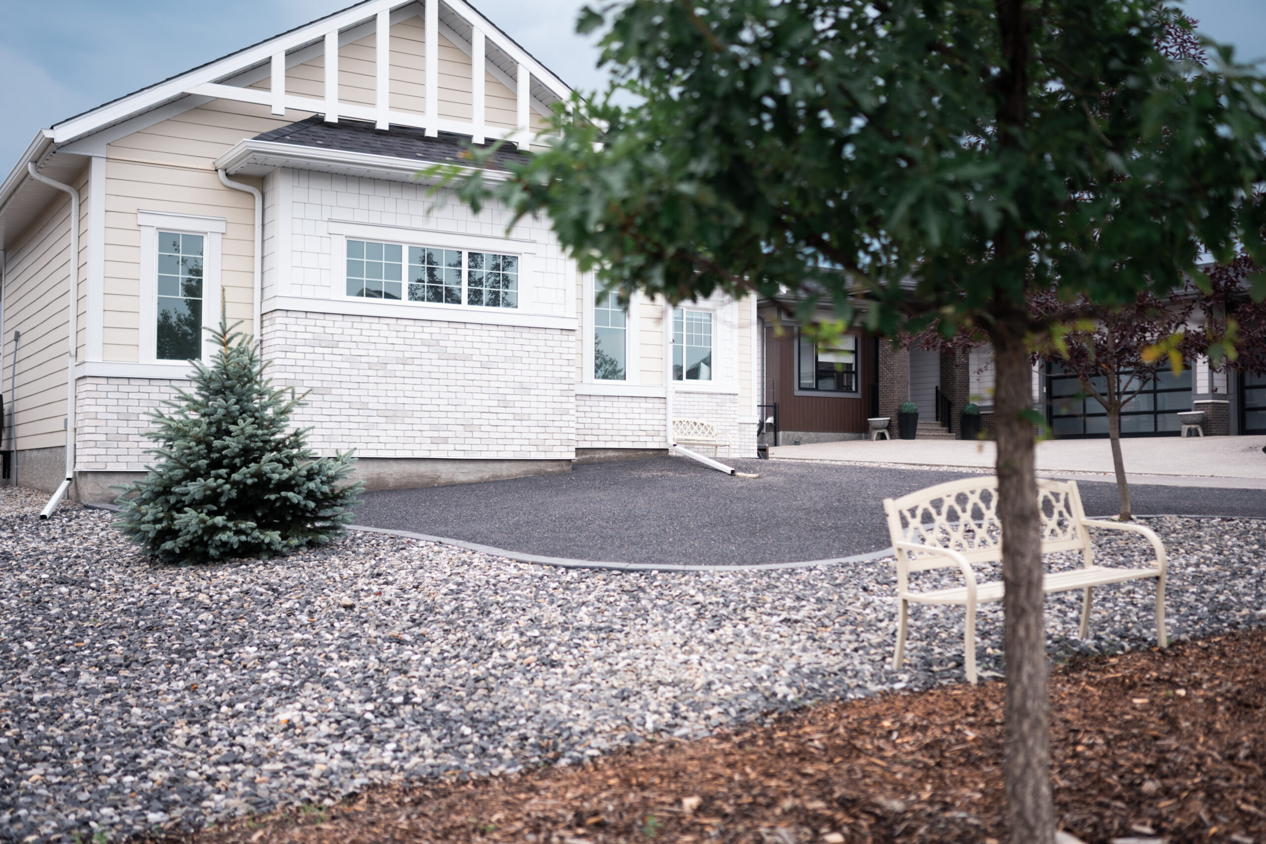 Cimarron Estates 4 landscaping featuring a modern home, gravel front yard, ornamental tree, and decorative seating area in Okotoks.