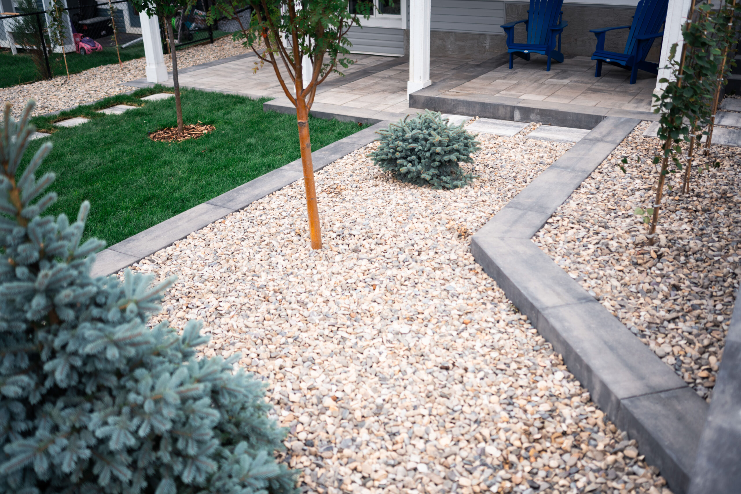 Landscaped residential yard in Okotoks featuring stone pathways, xeriscape design with gravel and shrubs, and a green lawn area.