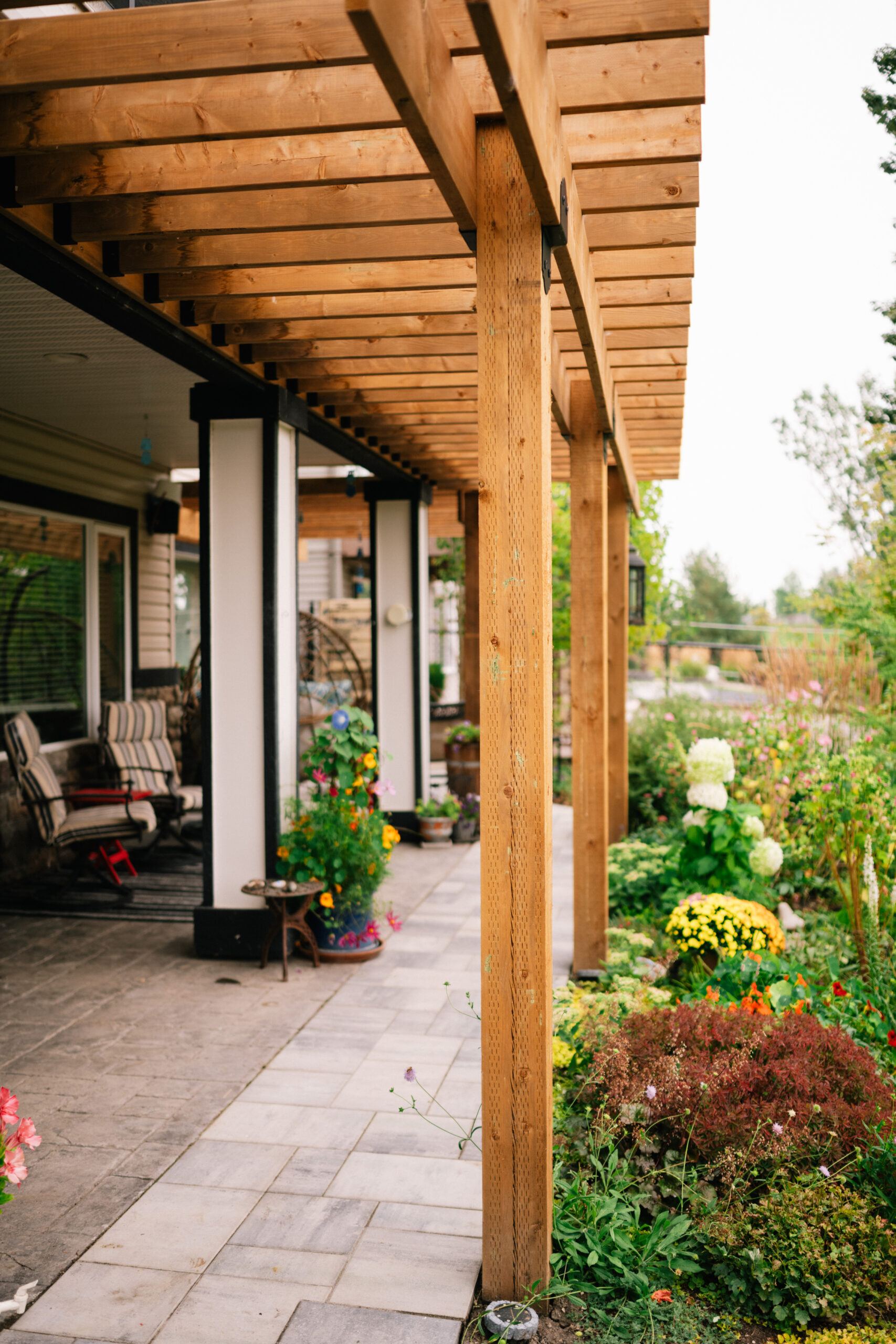Wooden pergola with stone walkway and vibrant flower beds in a residential landscaping project, showcasing outdoor living space and garden design in Okotoks.