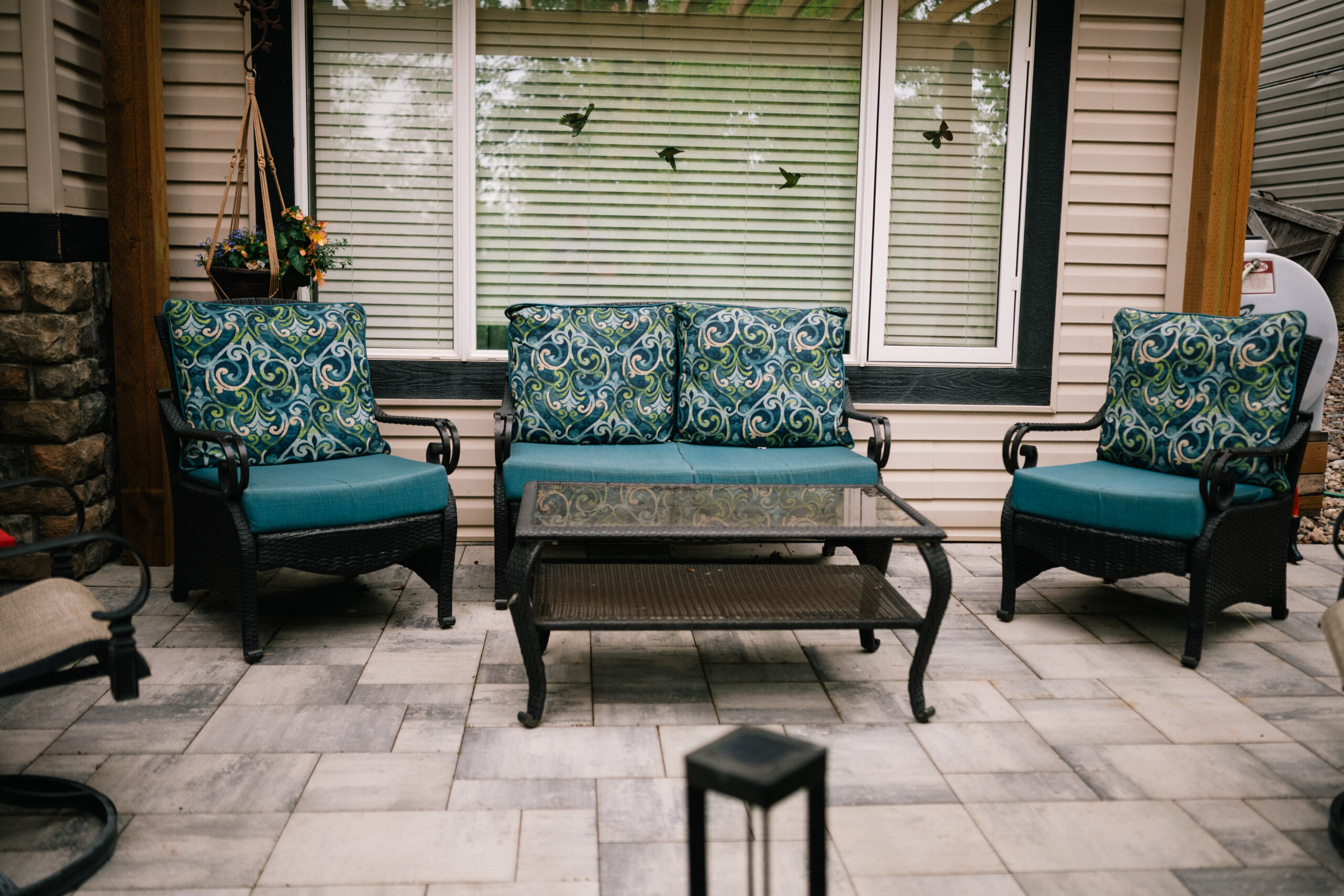 Seating area with patterned cushions, glass-top table, and stone patio, showcasing outdoor living space in a residential landscaping project by Kayben Landscaping in Okotoks.