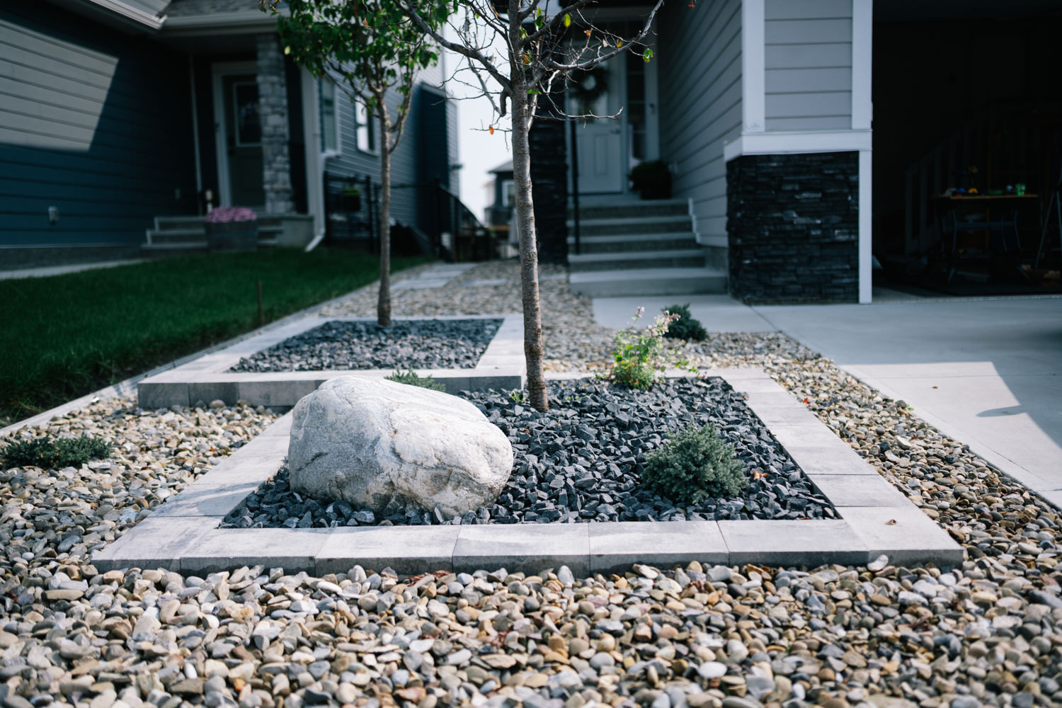 Landscaped front yard featuring stone pathways, decorative rock beds, and small trees, highlighting xeriscape design elements in a residential setting.