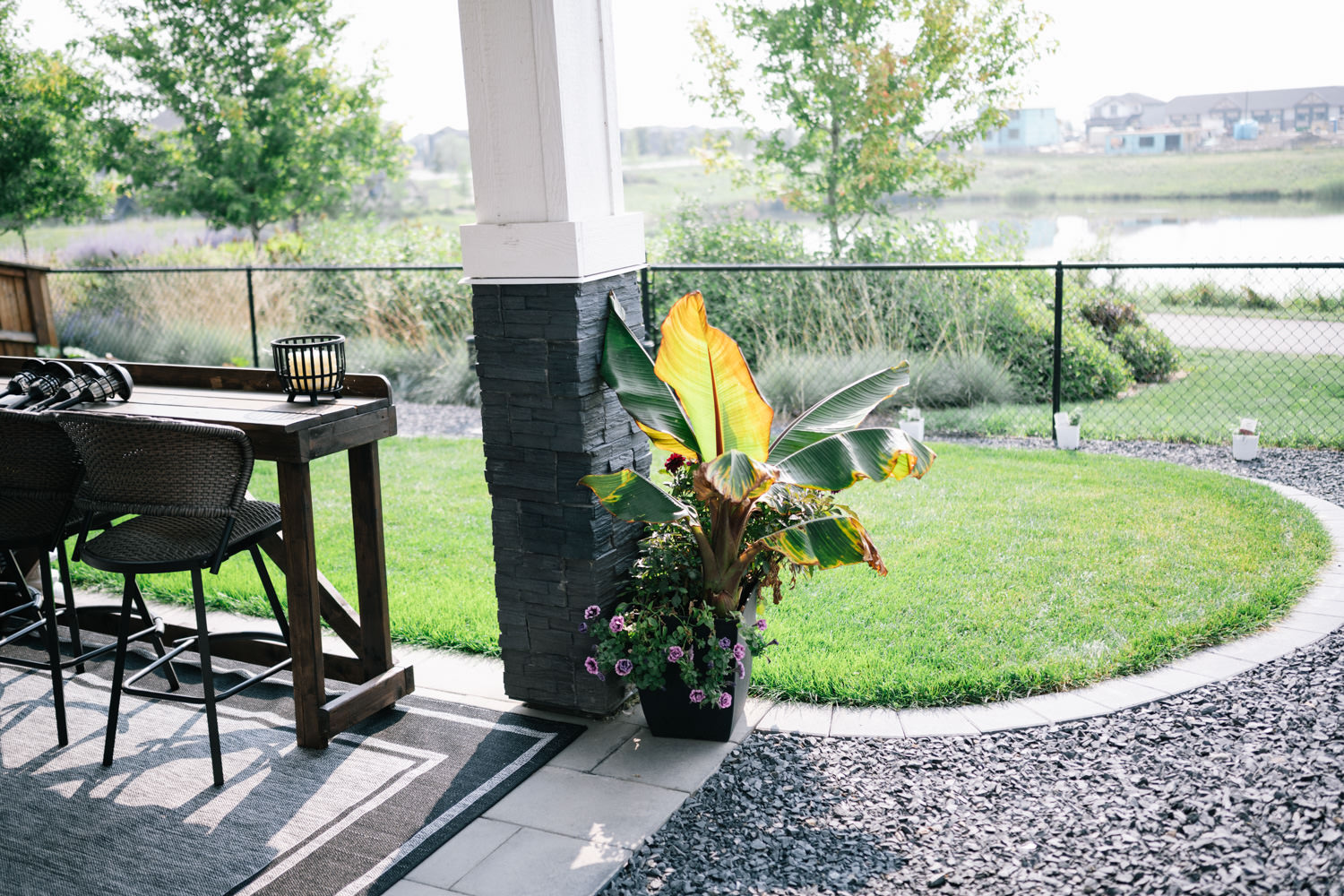 Seating area with wooden table and chairs, surrounded by lush greenery and decorative plants, showcasing a landscaped outdoor space in D’Arcy Ranch, Okotoks.
