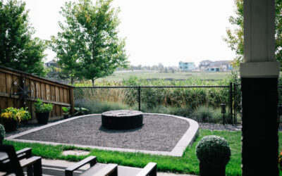 Landscaped backyard with fire pit, gravel area, surrounding trees, and fenced view of green space, showcasing residential design by Kayben Landscaping.